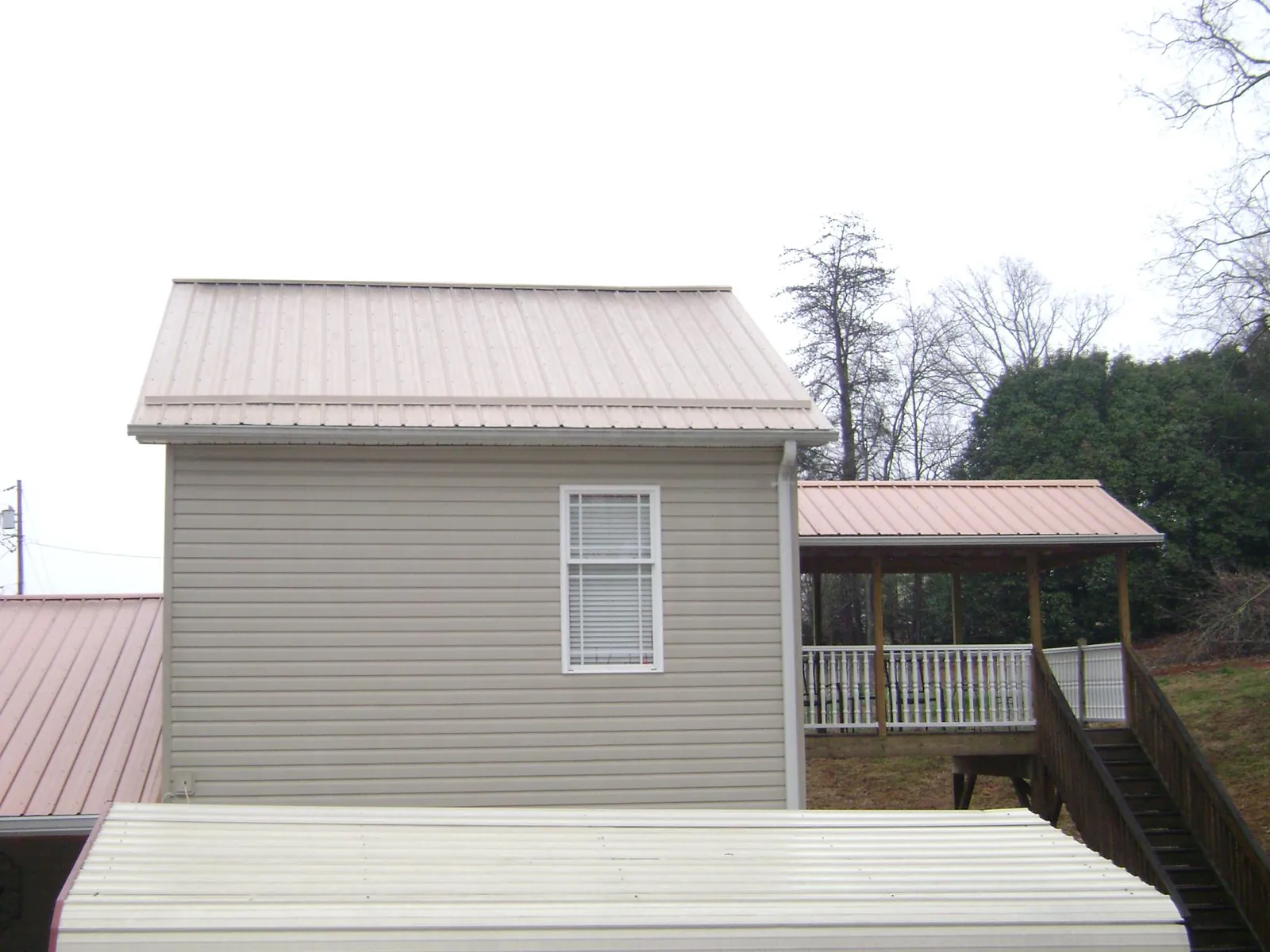 Tan metal roofs on a two story addition and attached porch, from a Roof Replacement job in Northwood
